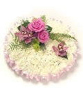 Massed funeral posy with white chrysanthemums, pink ribbon edging, and a pink focal, complemented with foliage.